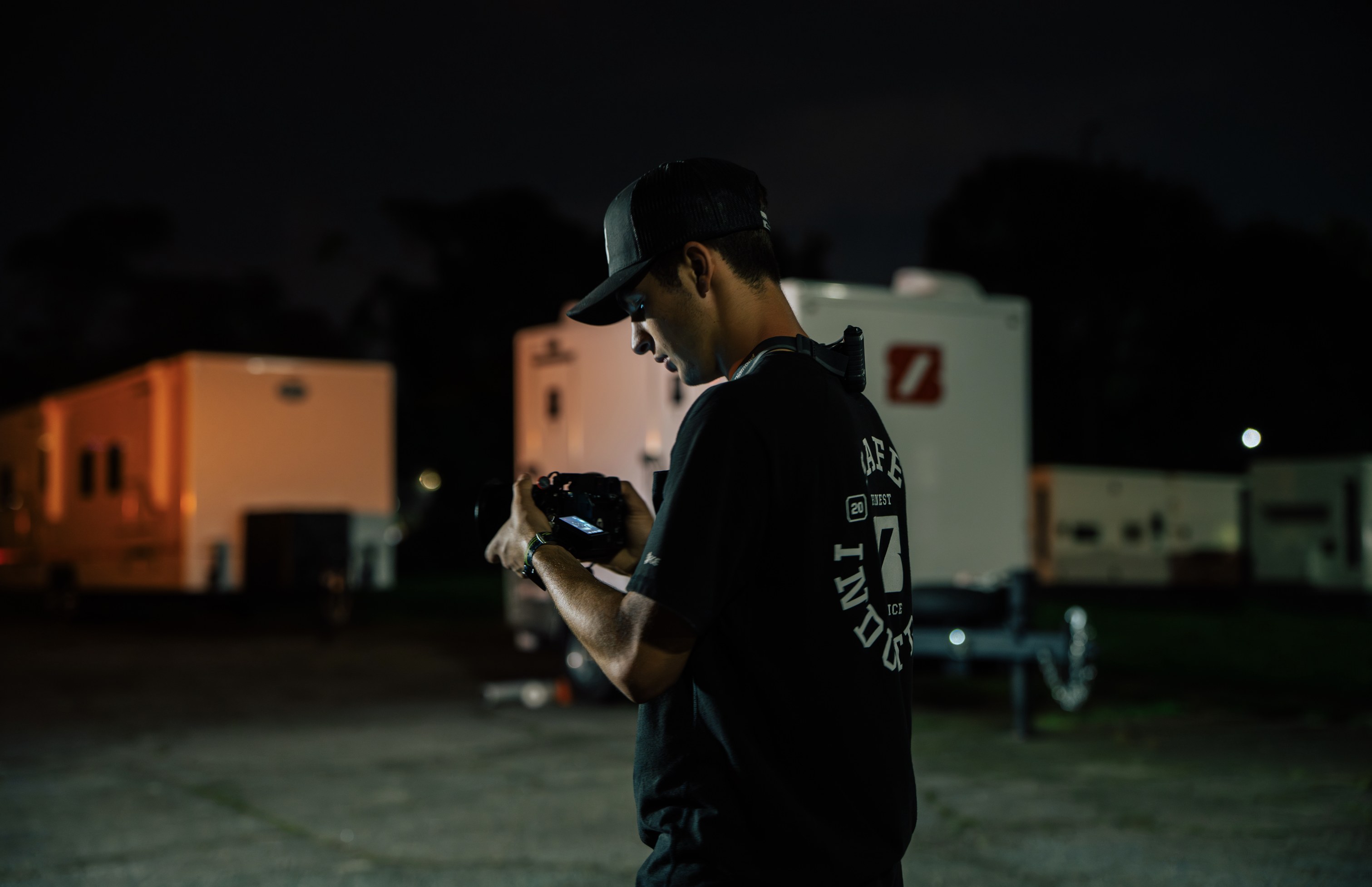 A young Safe Industries shooter checking a frame at night, emergency response trailers staged behind him