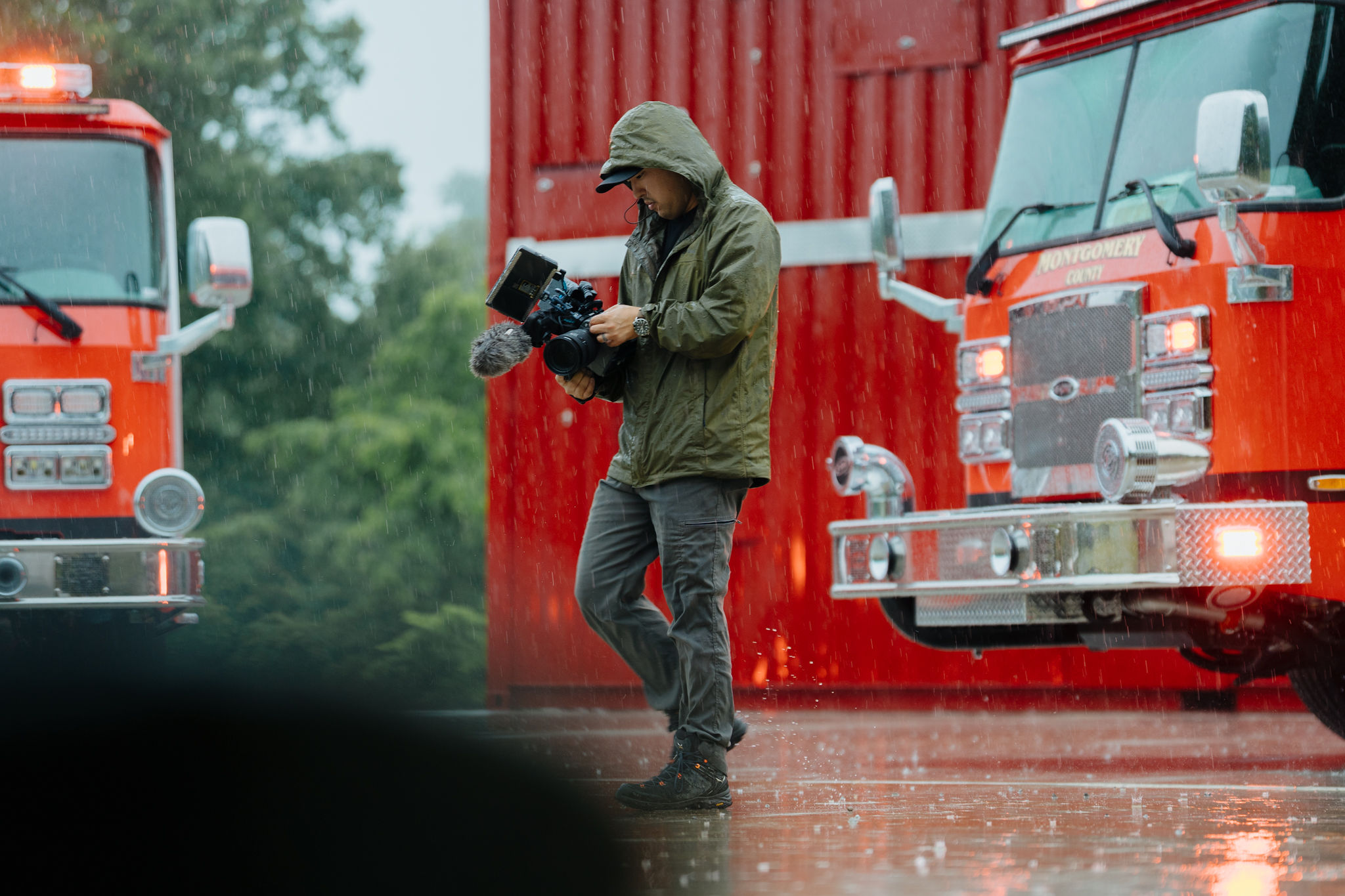 A cameraman working in pouring rain between two fire engines
