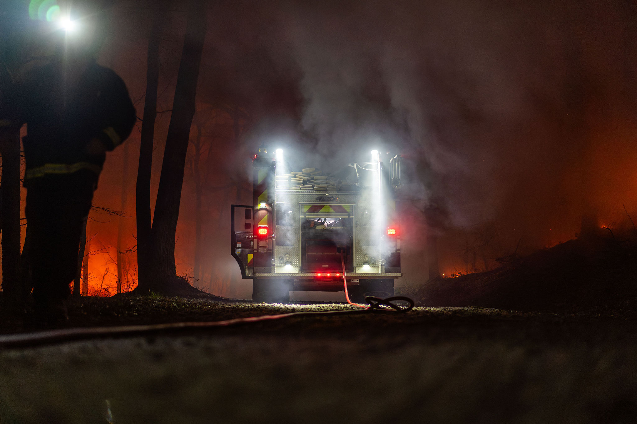 An engine working a night wildfire, hose line lit through the smoke